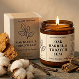 Candle labeled 'Oak Barrel & Tobacco Leaf' from Nature Skin Shop with packaging and natural elements on a neutral background.