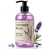A bottle of Nature Skin Shop Lavender Relax Therapeutic Ritual Wash, featuring a black pump and a beige label with black text and botanical illustrations. The bottle is filled with lavender-colored liquid and is styled with fresh lavender sprigs on a clean white background.