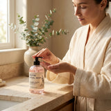 Woman in a bathrobe applying soap from a bottle labeled 'Repose' in a bathroom setting.