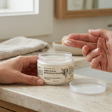 A person applies cream from a clear jar labeled Nature Skin Shop Structural Resilience Mask to their lips in a bright bathroom setting.