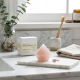 Pink soap on a marble surface with a plant, box, and towel in the background
