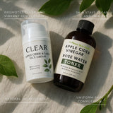 Two skincare products, a face cream and a toner, on a light surface with leaves around.