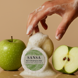 SANSA ACV Shampoo Bar with a hand applying soap, an apple, and a halved apple on a beige background
