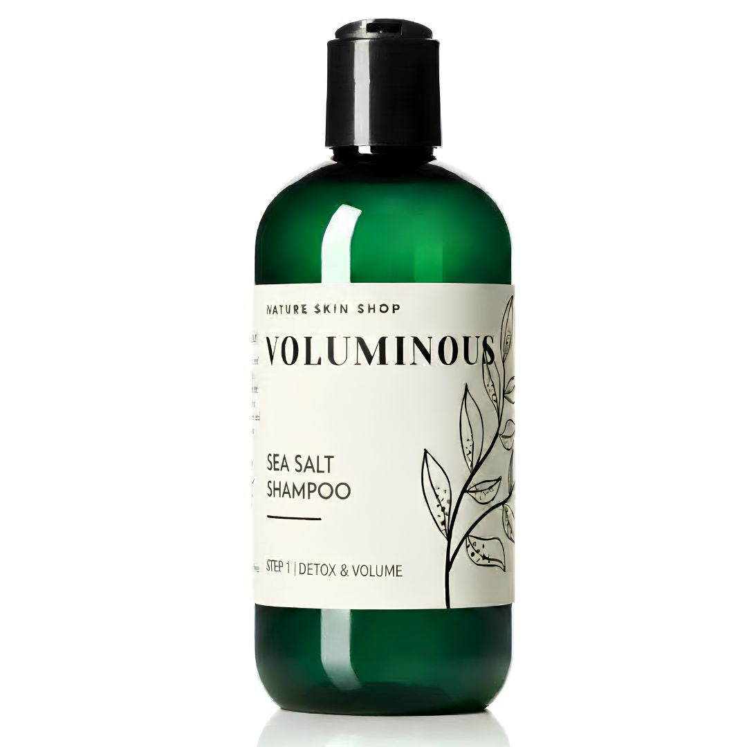 A bottle of Nature Skin Shop Voluminous Sea Salt Shampoo in a translucent dark green bottle with a black cap and a white label featuring botanical illustrations.