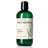 A bottle of Nature Skin Shop Voluminous Sea Salt Shampoo in a translucent dark green bottle with a black cap and a white label featuring botanical illustrations.