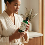 Woman in a robe holding a green bottle of Shikakai Eartha hair product.