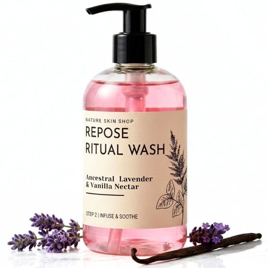 A bottle of Nature Skin Shop Repose Ritual Wash with pink liquid, a black pump, and a beige label, styled with lavender sprigs and a vanilla bean on a white background.