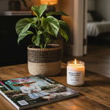Candle labeled 'Smoke & Cigar Eliminator' next to a plant and magazine on a wooden surface.