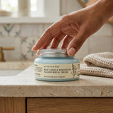 Hand opening a jar of cream on a bathroom counter