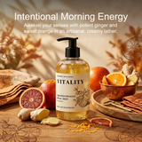 A bottle of Vitality Natural Wash by Nature's Skin Shop is centered on a wooden surface, surrounded by ginger roots, citrus slices, and dried botanical elements. The image includes promotional text at the top reading 'Intentional Morning Energy' and 'Awaken your senses with potent ginger and sweet orange in an artisanal, creamy lather.