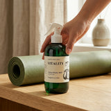 Hand holding a bottle labeled 'Vitality Yoga Ritual Mist' with a yoga mat in the background.