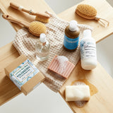 Bath products including bottles, soap, and brushes on a wooden tray.