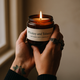 Candle labeled 'Whiskey and Tobacco' held by a person with a tattoo.