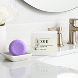 Purple bath bomb and packaging labeled 'ZOE' on a bathroom counter.